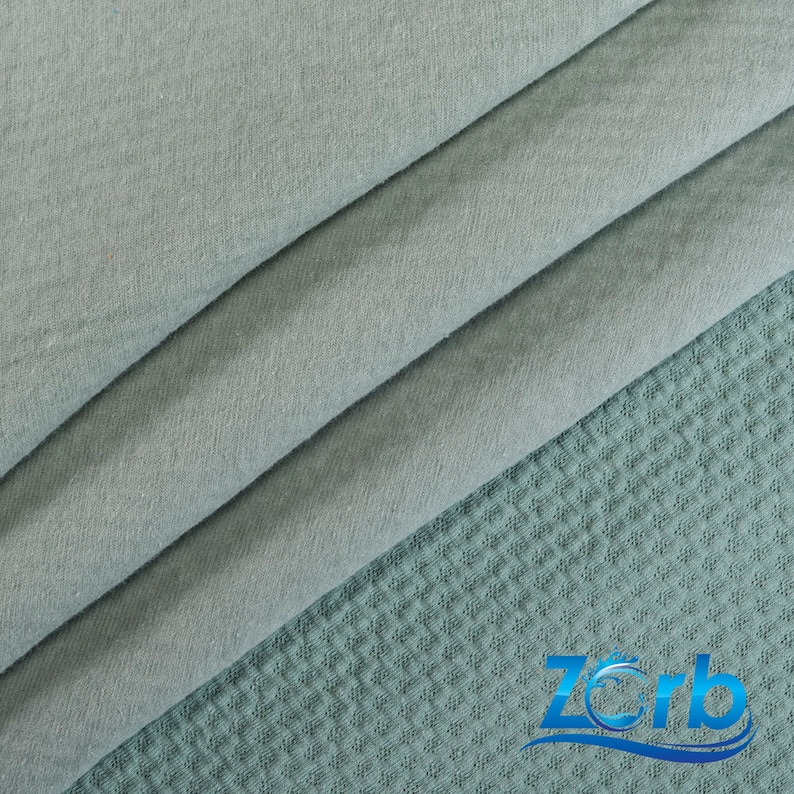 May include: A close-up of a light blue fabric with a waffle texture. The fabric is folded in thirds, with the top layer folded over the bottom two layers. The fabric is soft and smooth to the touch.
