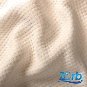 May include: Close-up of a white fabric with a textured pattern. The fabric is soft and has a subtle sheen. The fabric is labeled with the word "Zorb" in blue text.