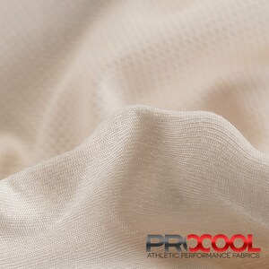May include: Close-up of a beige athletic performance fabric with a textured weave. The fabric is soft and breathable, making it ideal for activewear. The fabric is labeled "PRXCOOL ATHLETIC PERFORMANCE FABRICS".