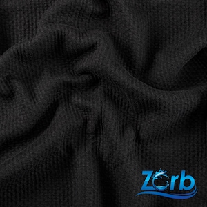 May include: Black waffle knit fabric with a textured surface. The fabric is folded and draped, showing the soft, plush texture. The fabric is a dark charcoal color.