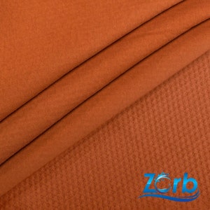 May include: Close-up of a rust-colored fabric with a textured underside. The fabric is soft and smooth on the top side and has a waffle-like texture on the bottom side.