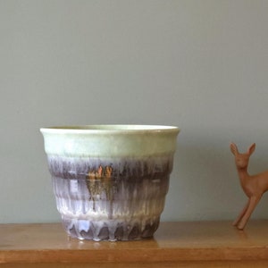 Può includere: Un grande vaso in ceramica smaltata con la parte superiore di colore verde chiaro e la parte inferiore smaltata in marrone, viola e bianco. Il vaso ha una forma arrotondata e un bordo leggermente svasato.