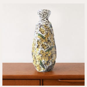 May include: A tall ceramic vase with a narrow neck and a textured, cratered surface. The exterior features a mottled glaze in shades of mustard yellow, dark brown, white, and hints of deep green, creating a rugged, uneven appearance throughout.