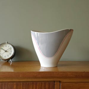 May include: A white ceramic vase with a gray and pink geometric design. The vase has a wide mouth and a narrow base.