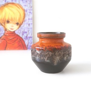 May include: A ceramic vase featuring a wide, rounded body with a short, flared neck. The glaze transitions from a smooth, dark brown base to a textured, mottled grey-brown midsection, topped with a vibrant, glossy orange rim and neck.