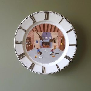Puede incluir: Reloj de pared de cerámica blanca con números romanos negros y borde negro. La esfera del reloj presenta una ilustración de una habitación con chimenea, personas y mascotas. Las manecillas del reloj son marrones.