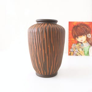 May include: A brown and black ceramic vase with a textured, wood-like design. The vase is about 10 inches tall.