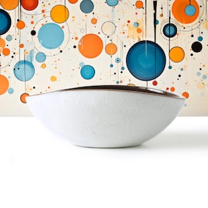 May include: A wide, shallow bowl with a speckled white exterior and a smooth, dark brown interior. The bowl features a curved, asymmetrical rim that dips slightly on the sides, creating a distinct oval shape. The surface has a matte texture.