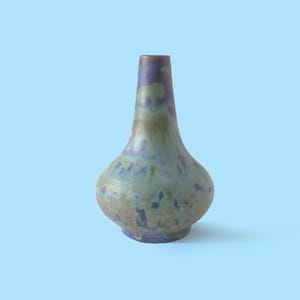 Può includere: Un vaso in ceramica con base bulbosa e collo stretto, caratterizzato da uno smalto maculato nelle tonalità del verde salvia, blu profondo e marrone terra. La superficie presenta una finitura liscia e lucida con sfumature di colore diffuse.