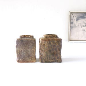 Peut inclure: Deux vases carrés en céramique avec une surface rugueuse et texturée dans des tons de brun et de vert.
