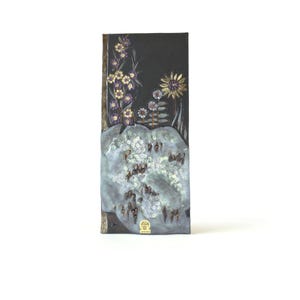 Può includere: Opera d'arte rettangolare con sfondo scuro ed elementi floreali. Mostra fiori viola e gialli e una base strutturata di colore chiaro. Il pezzo include un emblema dorato nella parte inferiore. Probabilmente è un oggetto decorativo.
