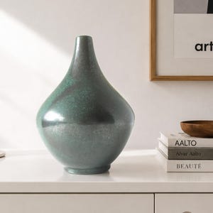 May include: A teardrop-shaped vase with a smooth, dark teal finish and a subtle mottled texture. The vase features a narrow neck that widens into a rounded base, standing as a singular decorative object with a reflective, glossy surface.