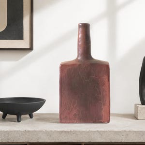 May include: A tall, rectangular ceramic vase with a narrow neck, featuring a deep reddish-brown finish and a distinct crackle glaze texture across its entire surface. The vase has a flat base and straight sides, presenting a weathered appearance.