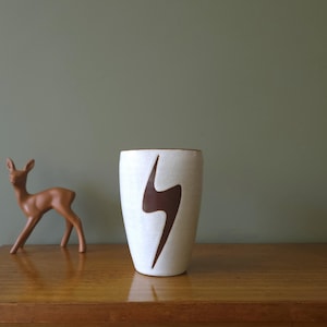 May include: White ceramic vase with a brown lightning bolt design. The vase is on a wooden surface.
