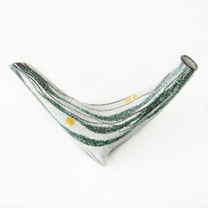 May include: A boomerang-shaped ceramic vase with a white base, adorned with green and black striped patterns. It has a small opening at one end and a rounded tip. Yellow dots are scattered across the surface. A decorative item.