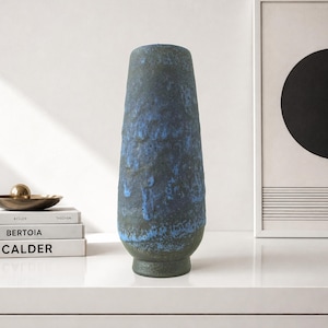 May include: A tall, tapered ceramic vase with a textured, dark charcoal gray surface featuring vibrant blue glaze drips running vertically down the sides. The vase has a narrow opening at the top and a slightly flared base, showcasing a rugged finish.