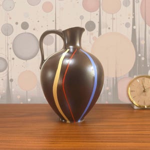 May include: A dark brown ceramic pitcher with a rounded body and a single handle. The surface features three vertical, curved painted stripes in yellow, red, and light blue that wrap around the front of the vessel, creating a colorful contrast.