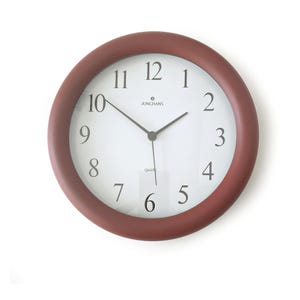 Può includere: Un orologio da parete rotondo con una cornice color terracotta opaco e un quadrante bianco. L'orologio presenta numeri arabi neri da 1 a 12, lancette nere per ore, minuti e secondi, e il testo JUNGHANS e quartz stampato in nero sul quadrante.