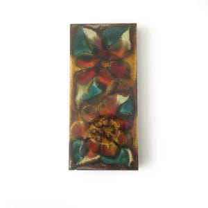 May include: A rectangular metal plaque featuring a vibrant enamel finish with two stylised floral motifs. The design incorporates deep red, teal, and golden-brown hues, creating a layered, glossy appearance with visible colour blending throughout.