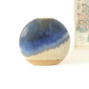 May include: A spherical ceramic vase with a gradient of colors. The top is a deep blue, transitioning to a lighter blue and then a beige base. The vase has a small opening at the top and a smooth, glossy finish.