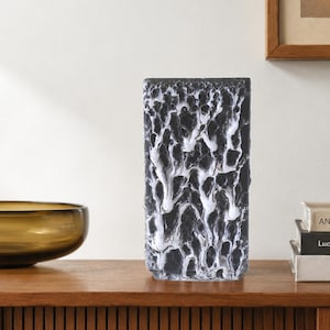 Op de afbeelding: Een rechthoekige vaas met een getextureerd oppervlak met een zwarte basiskleur en een wit druppelpatroon dat een contrastrijk, organisch effect creëert. Het object heeft een platte opening aan de bovenkant en een verticale oriëntatie.