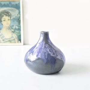 Op de afbeelding: Een kleine, bolvormige keramische vaas met een smalle hals. De vaas heeft een kleurovergang, van een donkergrijze basis naar een lichtblauw en wit gemarmerd patroon aan de bovenkant. Een decoratief item.