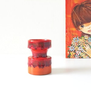 Puede incluir: Un jarrón de cerámica rojo y naranja con la parte superior acampanada y la base redondeada. El jarrón tiene un esmalte jaspeado de color rojo oscuro y naranja.