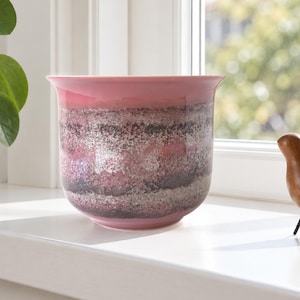 Pode incluir: Um vaso de cerâmica com borda alargada, apresentando um gradiente horizontal de texturas salpicadas em rosa, cinza escuro e prata metálica. O vaso tem um acabamento liso e brilhante com uma base arredondada para plantas.
