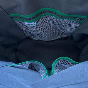 May include: The interior of a dark gray bag featuring a zippered pocket with a bright green trim and a white mesh compartment. A white label with the text moani is attached to the mesh. Two additional open mesh pockets with green trim are visible.