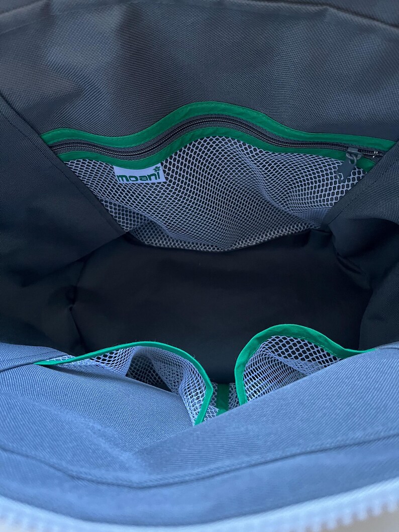 May include: The interior of a dark gray bag featuring a zippered pocket with a bright green trim and a white mesh compartment. A white label with the text moani is attached to the mesh. Two additional open mesh pockets with green trim are visible.