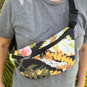 May include: A black fanny pack with a floral print featuring yellow, white, and orange flowers. The fanny pack has a black zipper and a black adjustable strap.