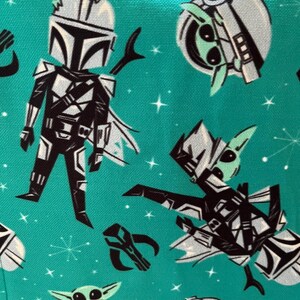 May include: A teal fabric featuring a repeating pattern of a black and white armored character with a helmet, a small green creature with large eyes, and a black helmet icon, all set against a background of small white stars and starbursts.