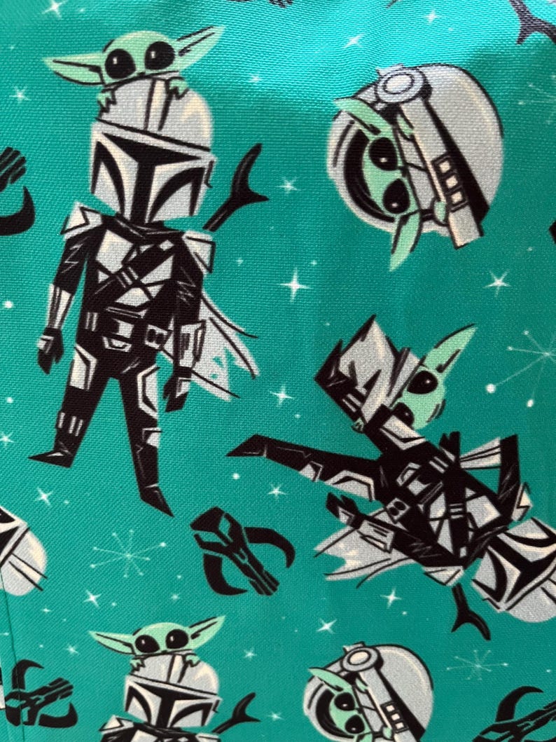 May include: A teal fabric featuring a repeating pattern of a black and white armored character with a helmet, a small green creature with large eyes, and a black helmet icon, all set against a background of small white stars and starbursts.
