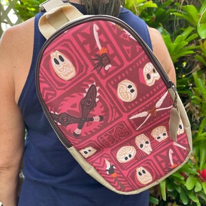 May include: A red and tan crossbody bag with a Polynesian-inspired print featuring tiki masks, spears, and other tribal designs. The bag has a zipper closure and a long adjustable strap.