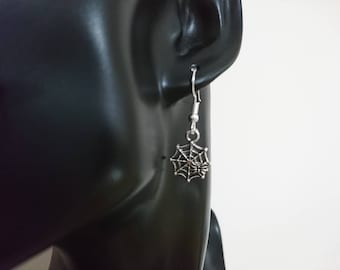 May include: Silver spiderweb dangle earrings with a small spider in the center. The earrings are on a black mannequin head.