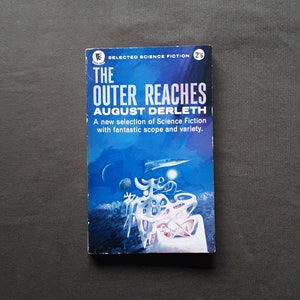 Op de afbeelding: Een paperback boekomslag met een blauwe en witte illustratie van een futuristische stad op een planeet met een blauwe lucht en een witte maan. De titel van het boek is "The Outer Reaches" door August Derleth. Het boek maakt deel uit van een serie genaamd "Selected Science Fiction".