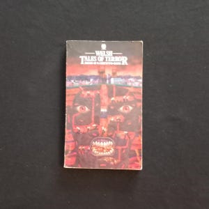 May include: A vintage paperback book titled "Welsh Tales of Terror." The cover features a grotesque, red-toned illustration of a face with large eyes and teeth, set against a cityscape background. The book is in good condition.