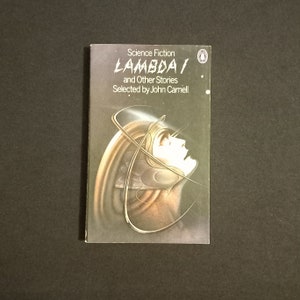 Peut inclure: Une couverture de livre de poche avec un fond noir et une illustration argentée d'une tête de personne avec un casque futuriste. Le titre du livre est "LAMBDA 1" et "Science Fiction" est imprimé au-dessus du titre. Le livre est intitulé "LAMBDA 1 et autres histoires" et l'auteur est "Sélectionné par John Carnell".