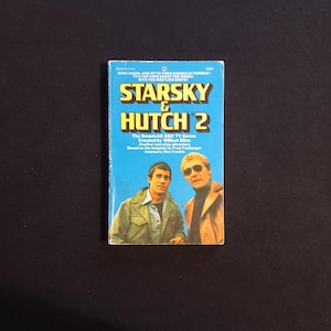 May include: A vintage paperback book titled "Starsky & Hutch 2" with a blue cover. The cover features images of two men and the text "The Smash-hit BBC TV Series". The book is set against a dark background.