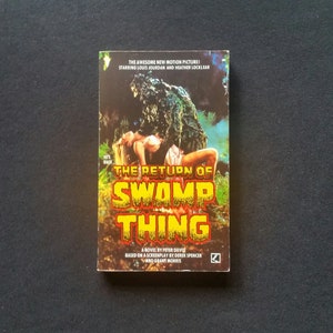 Puede incluir: Una portada de libro de bolsillo con un título amarillo y naranja "The Return of Swamp Thing". La portada muestra a una mujer con un vestido blanco que es sostenida por un monstruo verde del pantano.