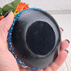 May include: A small, round dish with a black base and a blue and white polka dot pattern around the rim. The dish is being held in a hand.