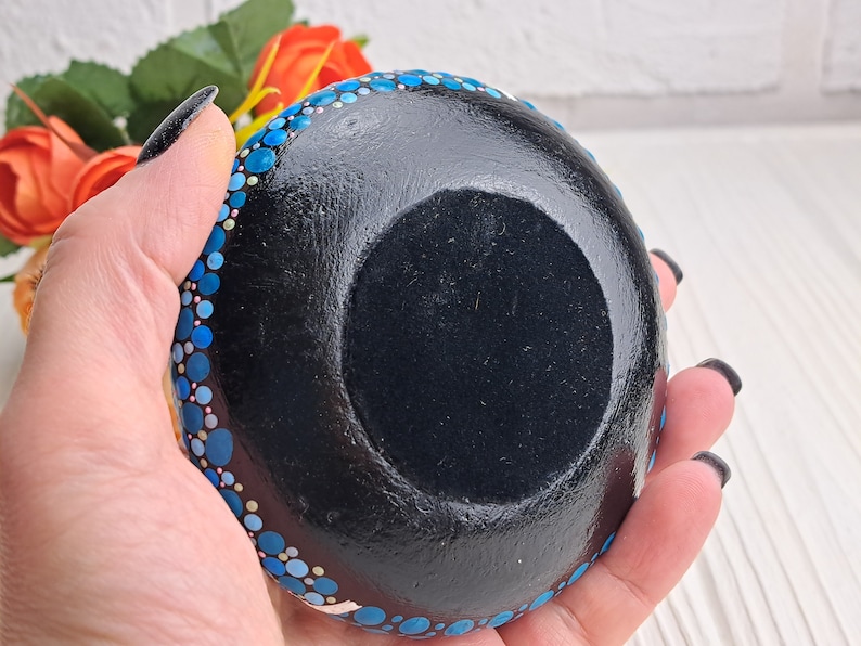May include: A small, round dish with a black base and a blue and white polka dot pattern around the rim. The dish is being held in a hand.