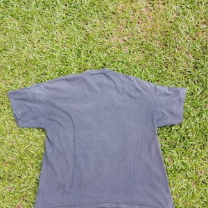 May include: A dark gray t-shirt with short sleeves. The shirt is lying flat on a green grassy surface.