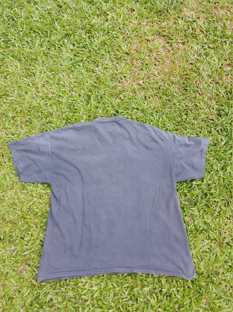 May include: A dark gray t-shirt with short sleeves. The shirt is lying flat on a green grassy surface.