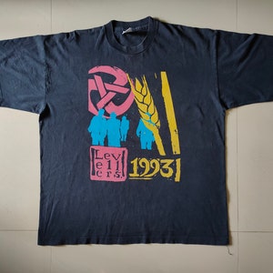 May include: Black t-shirt with a colourful graphic design featuring a wheat stalk, a symbol with three arrows, and the text "Levellers 1993".