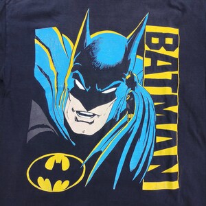 May include: A black t-shirt with a blue and yellow graphic of Batman's face and the word "BATMAN" printed vertically on the right side of the image.