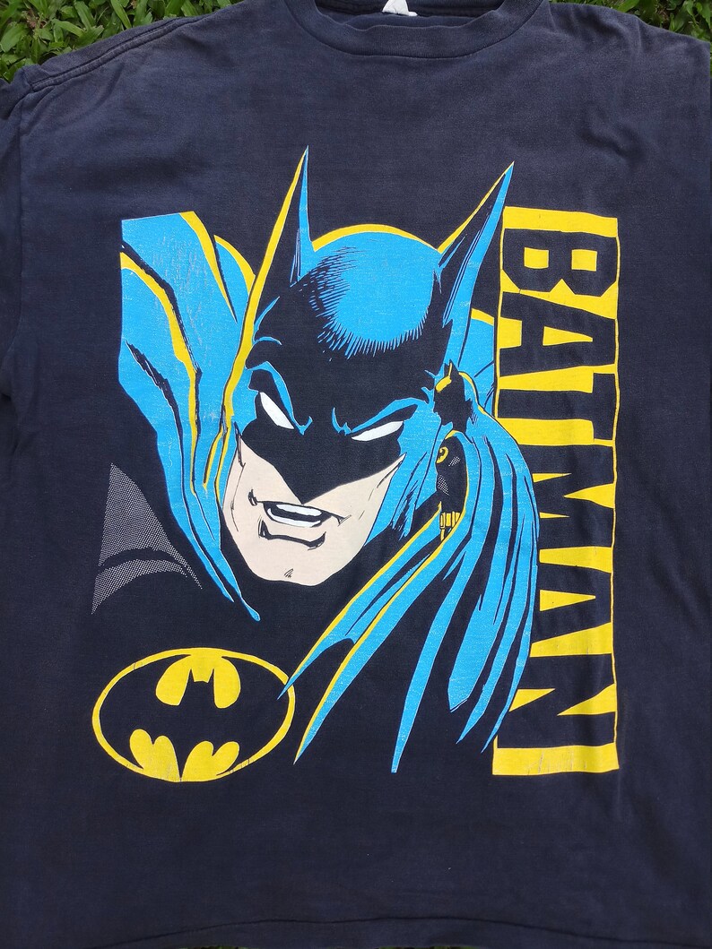 May include: A black t-shirt with a blue and yellow graphic of Batman's face and the word "BATMAN" printed vertically on the right side of the image.