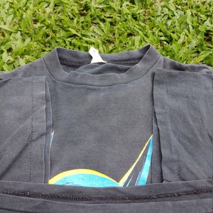 May include: A black t-shirt with a blue and yellow Batman logo printed on the front. The shirt is folded in half and the logo is partially visible.