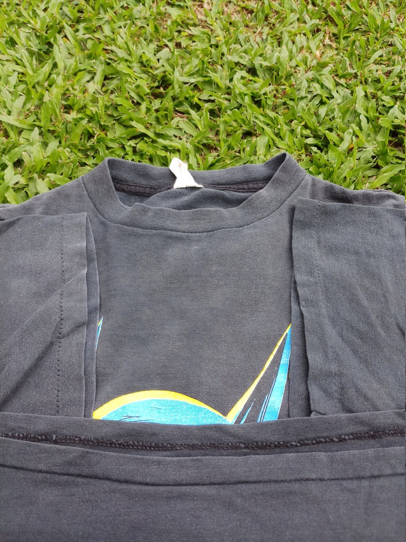 May include: A black t-shirt with a blue and yellow Batman logo printed on the front. The shirt is folded in half and the logo is partially visible.