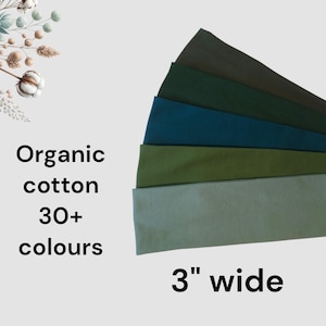 May include: A set of five fabric headbands in varying shades of green and blue, stacked in a fan shape. The text reads Organic cotton 30+ colours and 3" wide. The headbands are displayed next to a decorative illustration of cotton bolls.